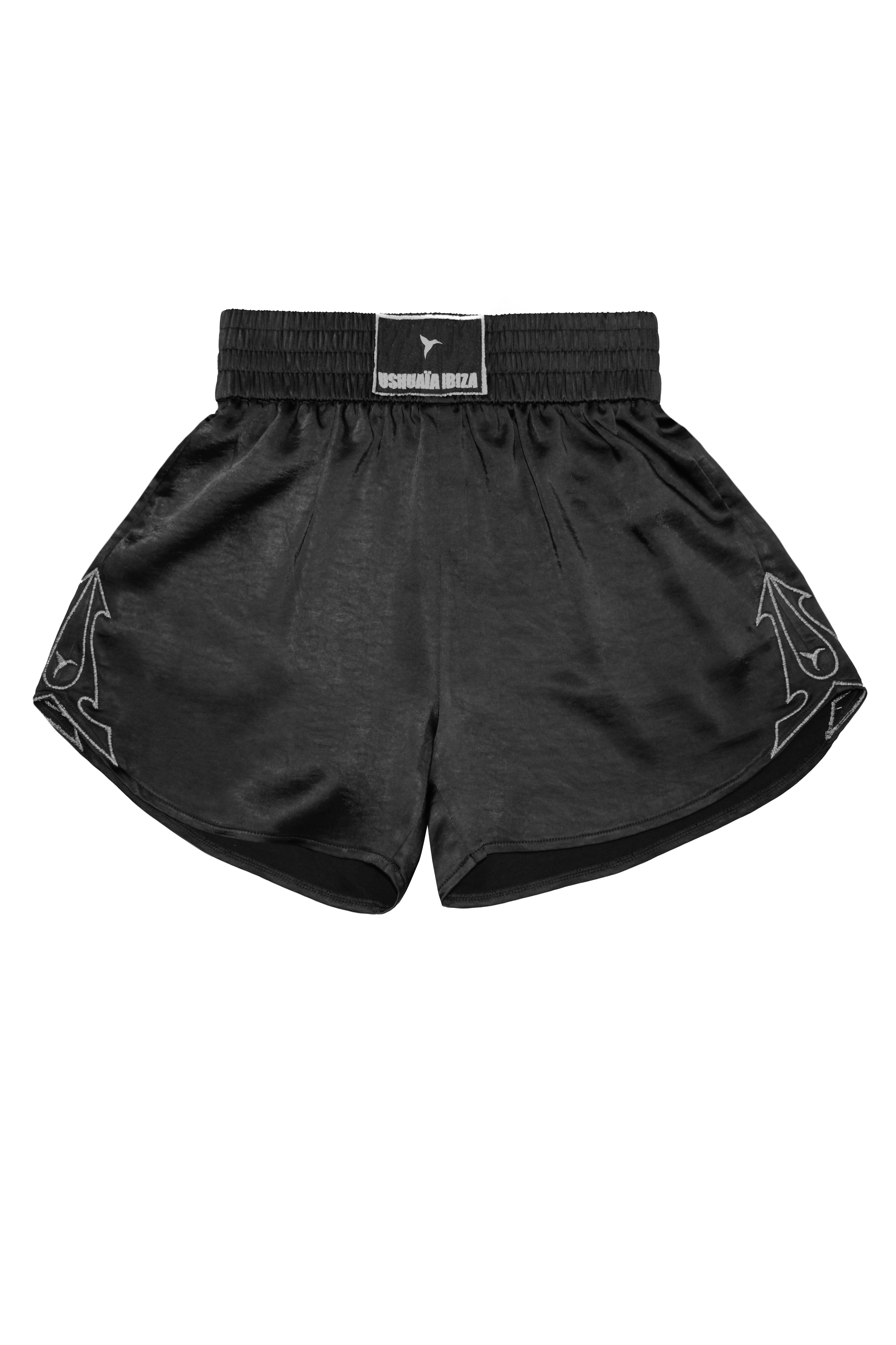 Satin-style black shorts with elastic waist and metallic finish. Perfect for bold summer looks in Ibiza. Shop now!