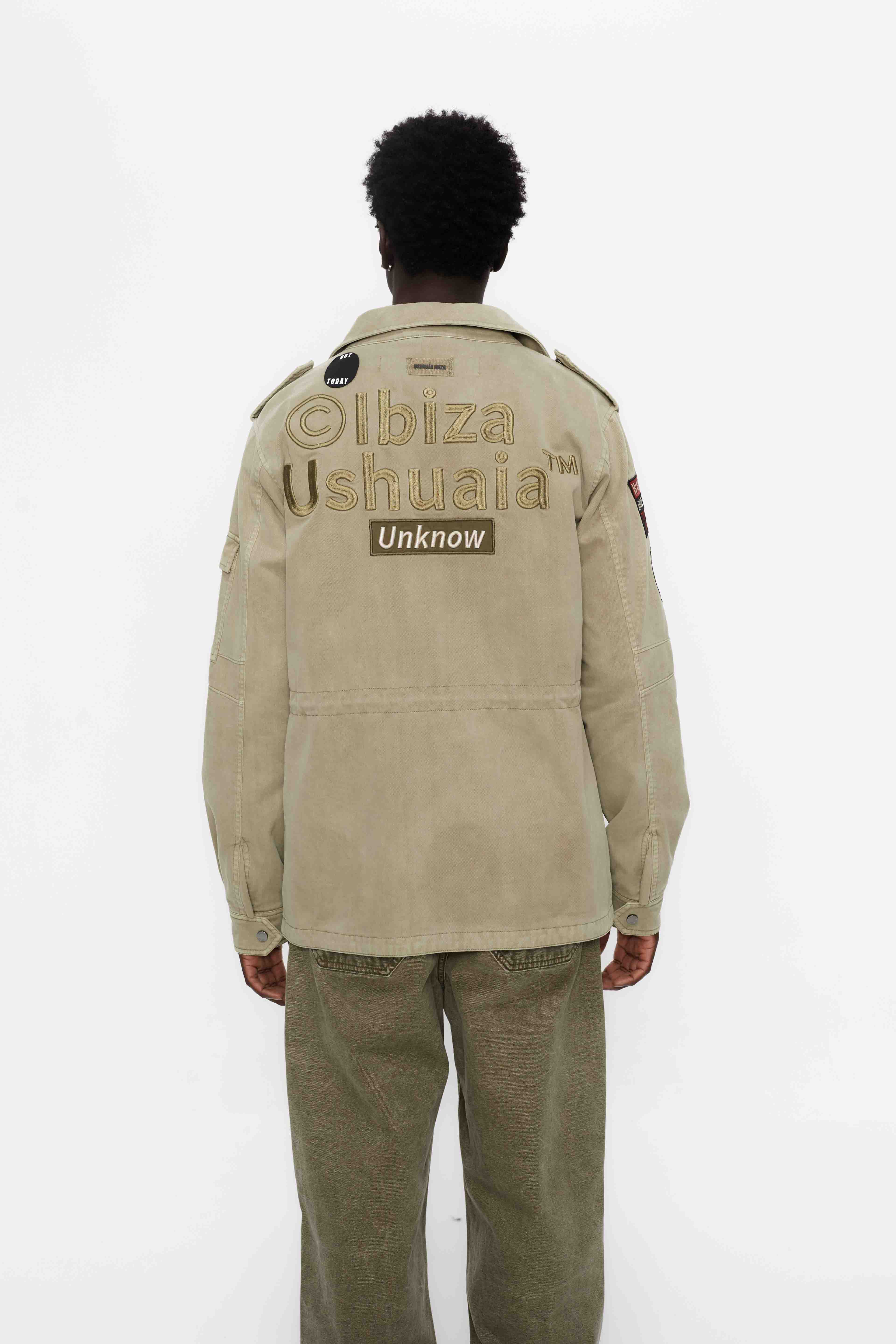 Washed twill military jacket with shirt collar and long sleeves with adjustable cuff with button. Central zip closure with adjustable drawstring at the waist. Patch pockets and flap on the front and sleeve. Combination of patches and embroidered application on front and back. Custom label detail on the back.