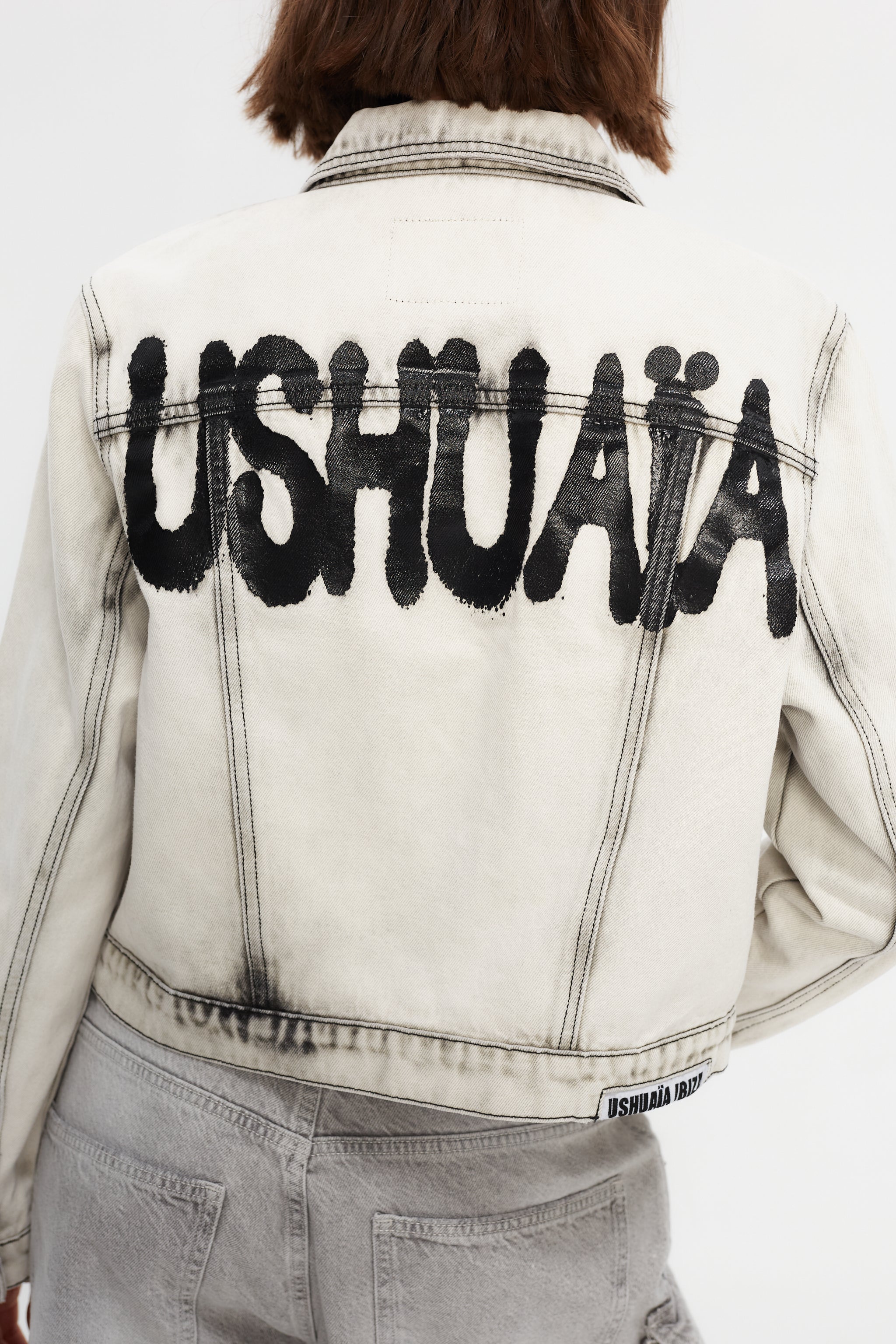 Cropped denim jacket with lapel collar and long sleeves, washed with a fade-out effect. Front closure with metal buttons. Features embroidery detail on the front and contrast combined print on the back.