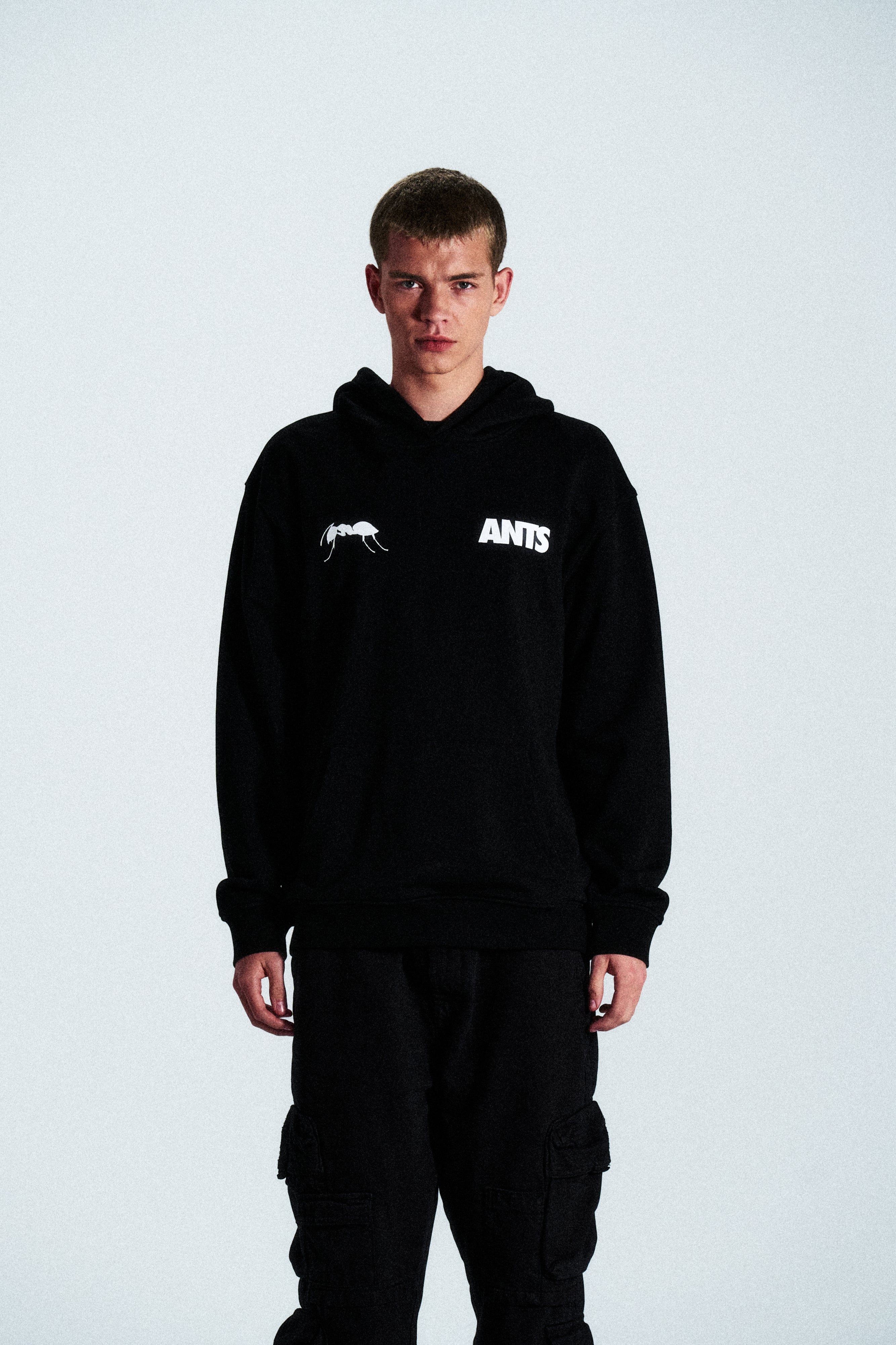 The Built Stronger Hoodie is crafted from French Terry Cotton. The black hoodie is emblazoned with a white ANTS logo on the front and features artwork on the back. A unique piece of merchandise and a versatile addition to any outfit.