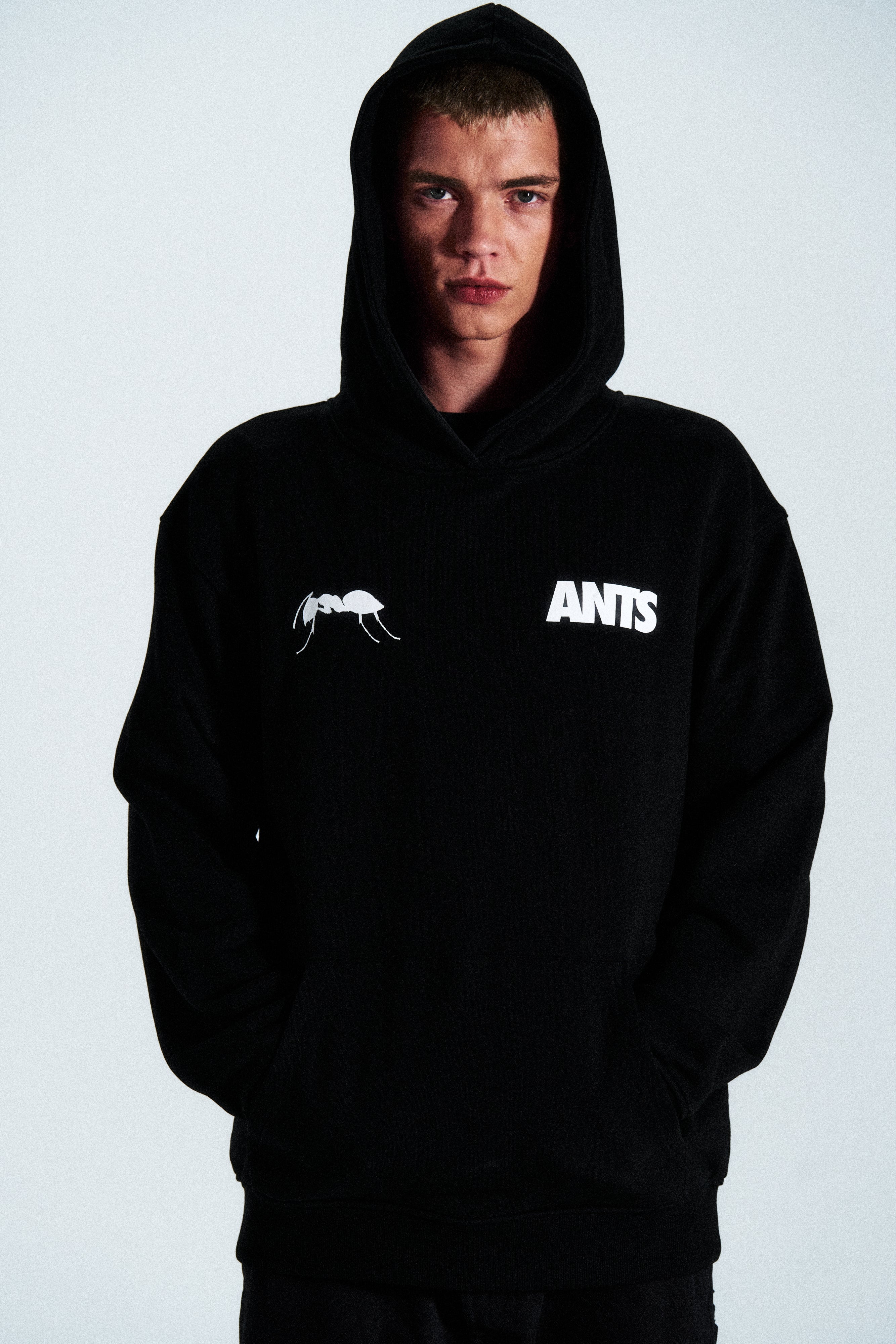 The Built Stronger Hoodie is crafted from French Terry Cotton. The black hoodie is emblazoned with a white ANTS logo on the front and features artwork on the back. A unique piece of merchandise and a versatile addition to any outfit.