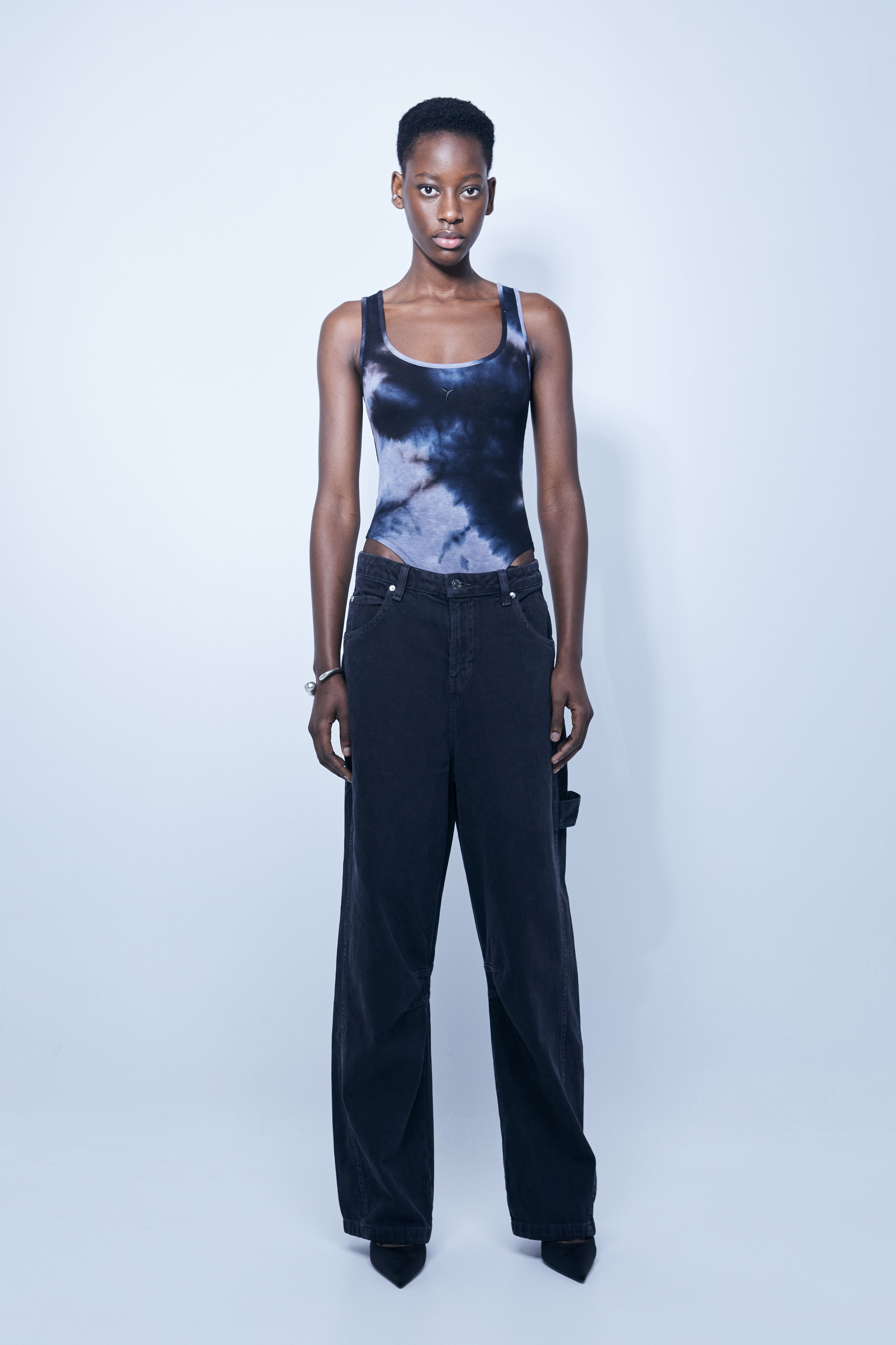 Washed rib bodysuit with tie-dye effect. Round neckline and straps. Embroidery detail on the front. Bottom closure with snap buttons.