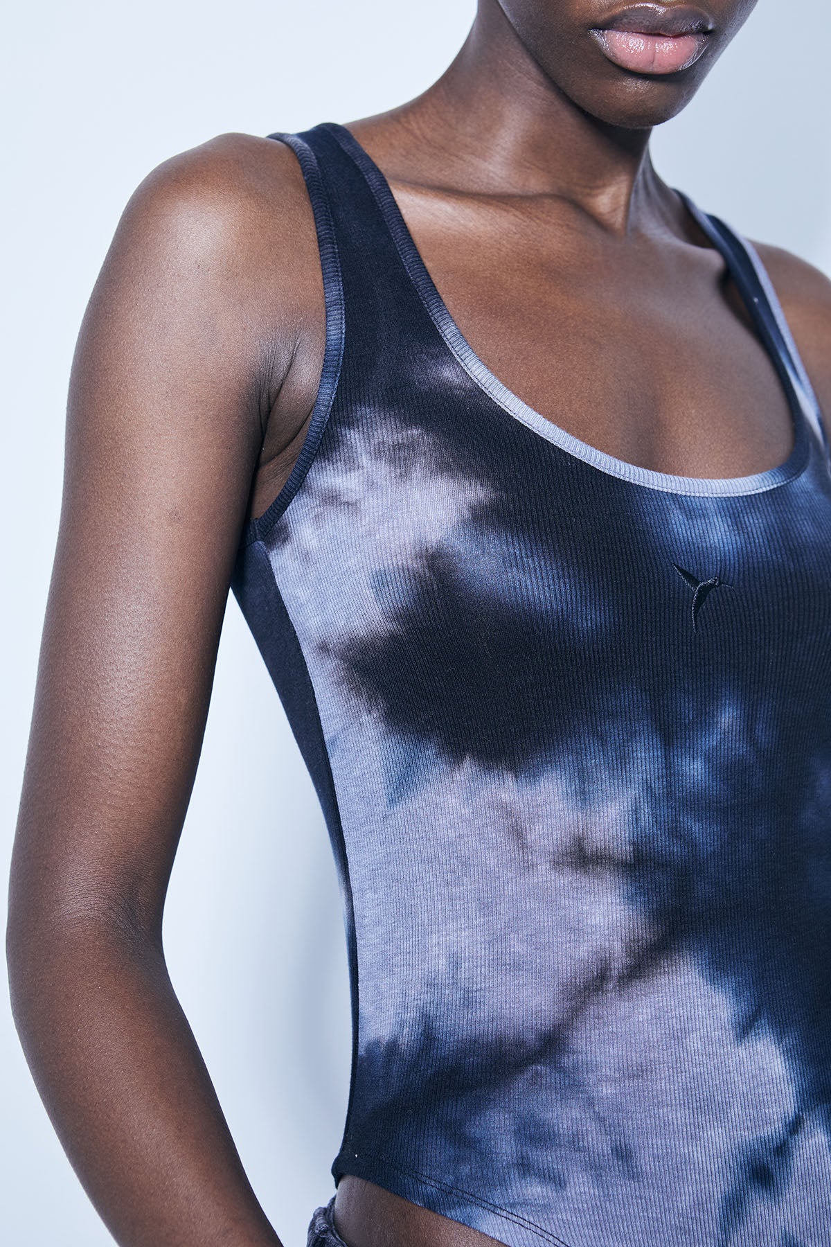 Washed rib bodysuit with tie-dye effect. Round neckline and straps. Embroidery detail on the front. Bottom closure with snap buttons.