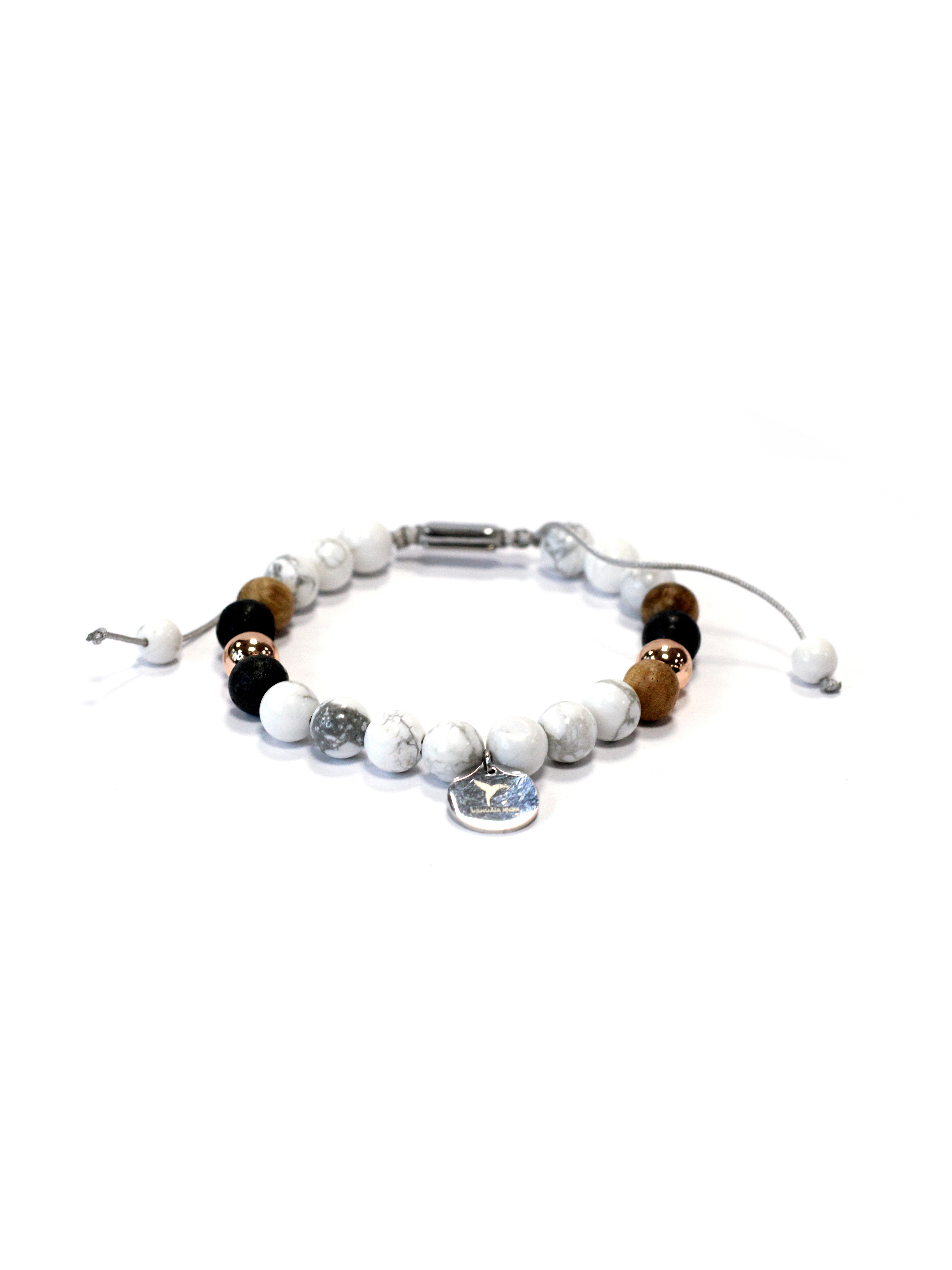 Adjustable bracelet with textile cord. Round beads in white marble, wood, black, and metallic accents. Circular metal charm with engraved logo. Unisex design.
COMPOSITION:
marble-effect resin, wood, natural stone, metal alloy, textile cord.