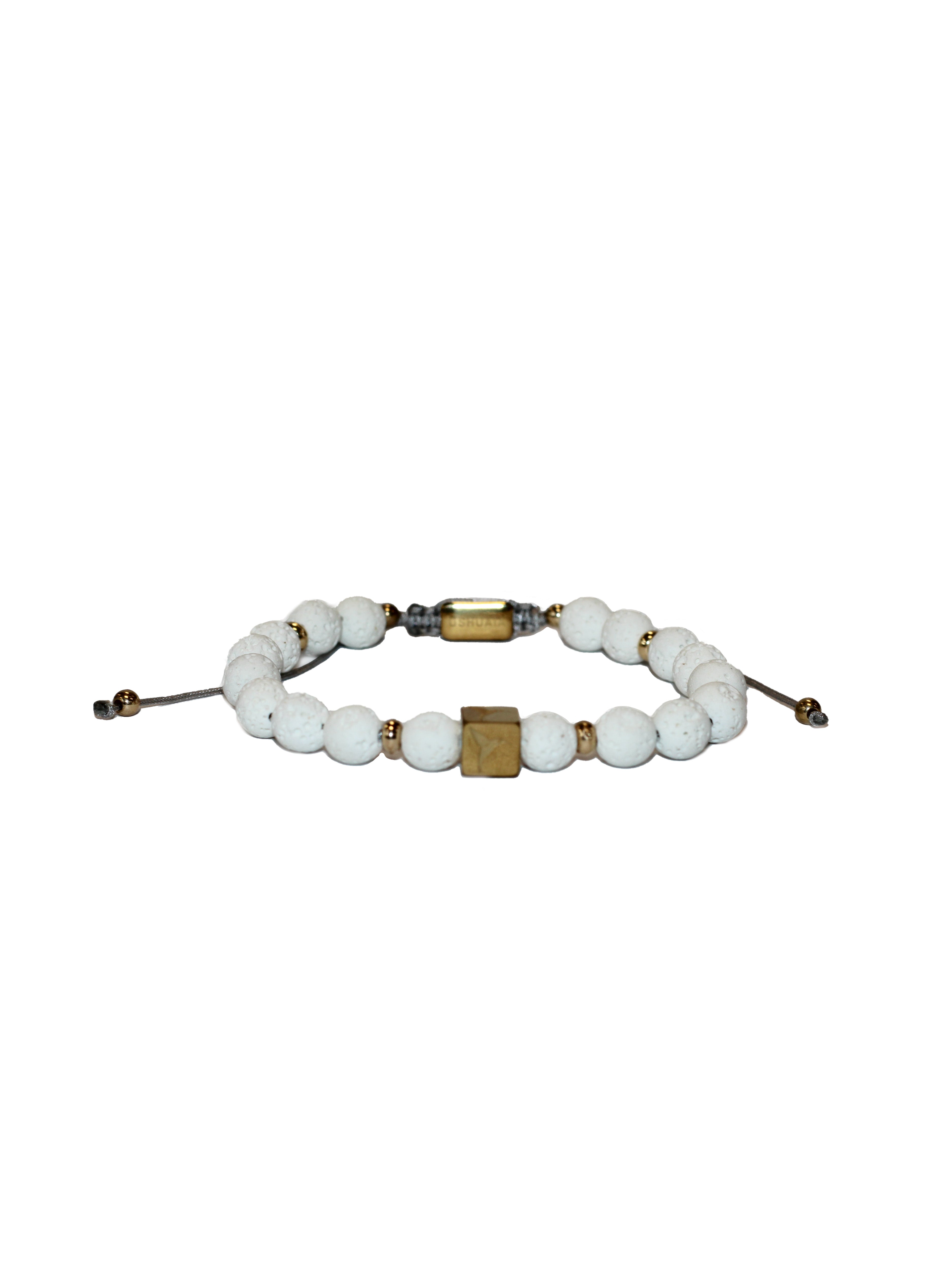 Adjustable bracelet with textile cord. Round white volcanic stone beads with gold metallic accents. Central cube-shaped metal piece with engraved logo. Unisex design.
COMPOSITION:
volcanic stone, metal alloy, textile cord.