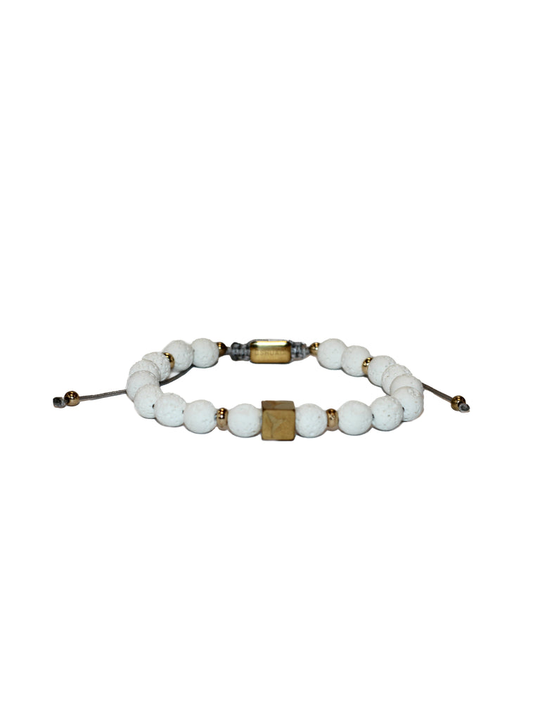 Adjustable bracelet with textile cord. Round white volcanic stone beads with gold metallic accents. Central cube-shaped metal piece with engraved logo. Unisex design.
COMPOSITION:
volcanic stone, metal alloy, textile cord.