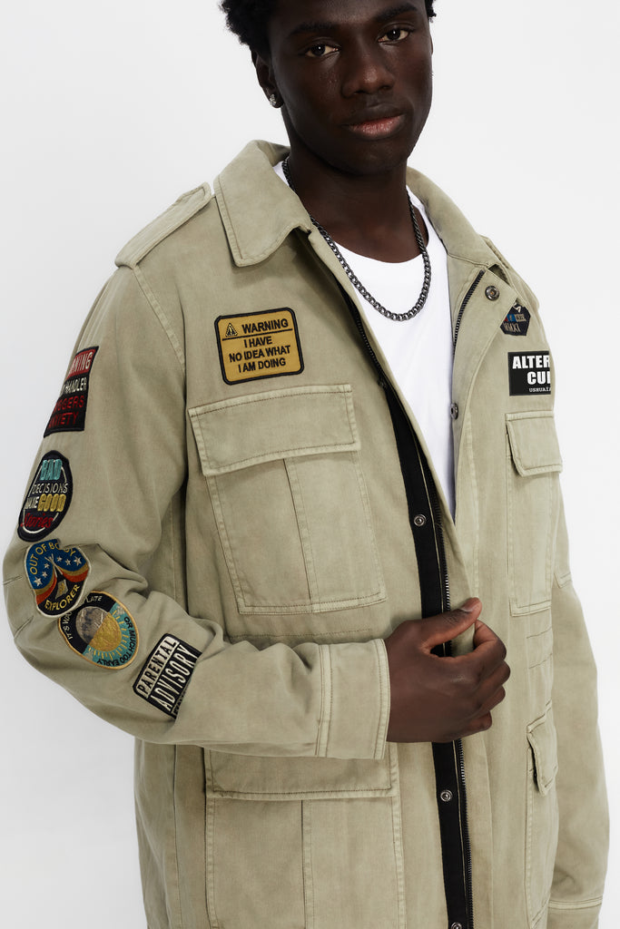 Washed twill military jacket with shirt collar and long sleeves with adjustable cuff with button. Central zip closure with adjustable drawstring at the waist. Patch pockets and flap on the front and sleeve. Combination of patches and embroidered application on front and back. Custom label detail on the back.
