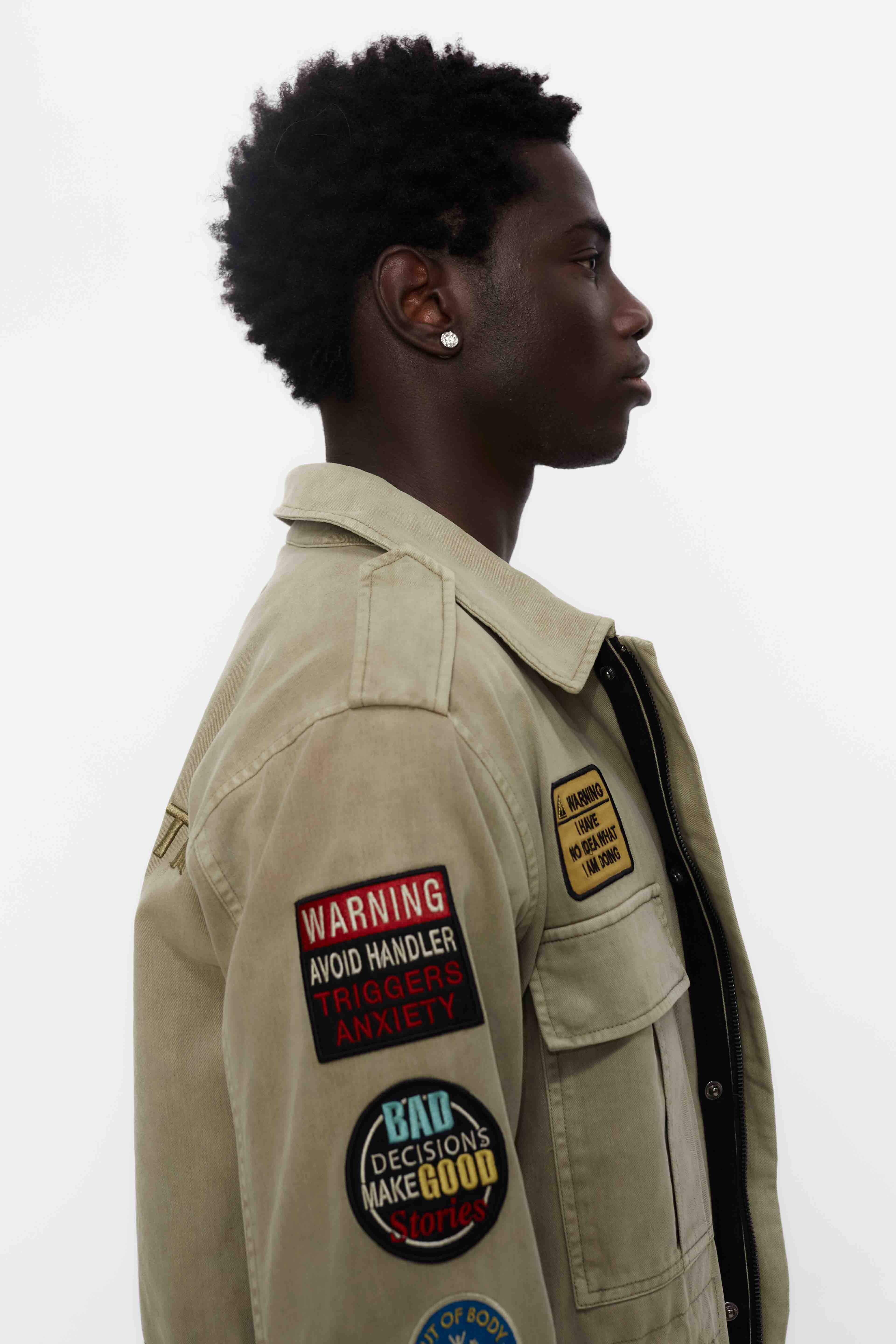 Washed twill military jacket with shirt collar and long sleeves with adjustable cuff with button. Central zip closure with adjustable drawstring at the waist. Patch pockets and flap on the front and sleeve. Combination of patches and embroidered application on front and back. Custom label detail on the back.