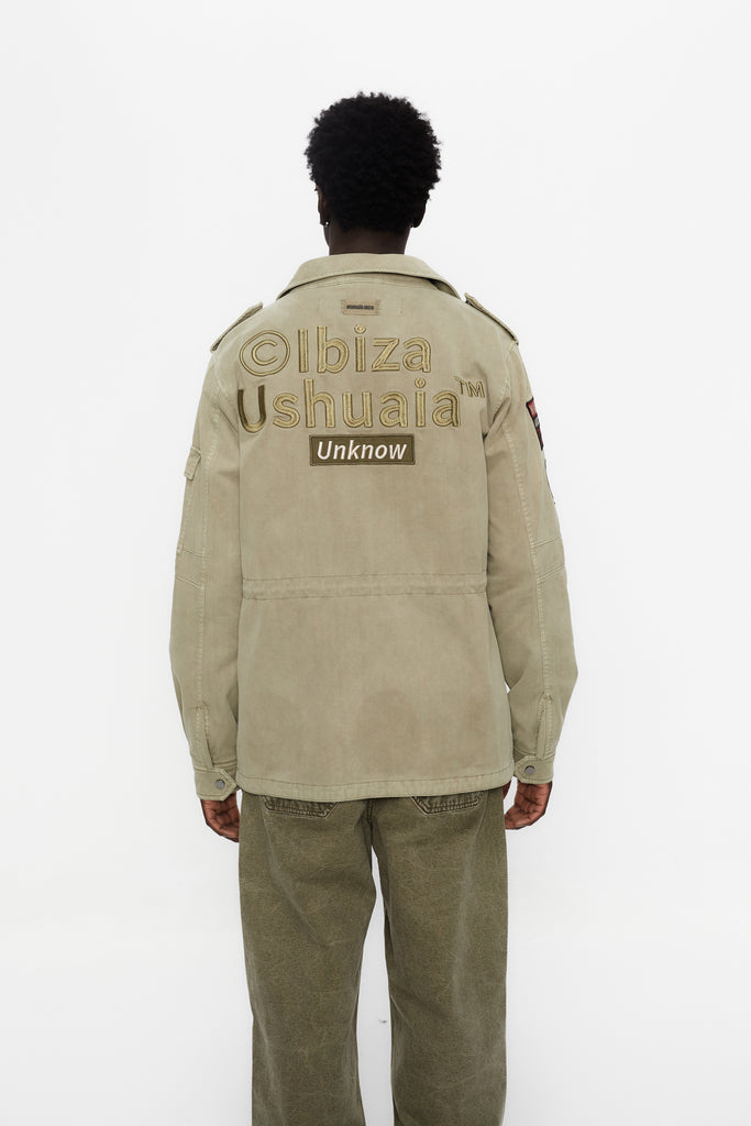 Washed twill military jacket with shirt collar and long sleeves with adjustable cuff with button. Central zip closure with adjustable drawstring at the waist. Patch pockets and flap on the front and sleeve. Combination of patches and embroidered application on front and back. Custom label detail on the back.