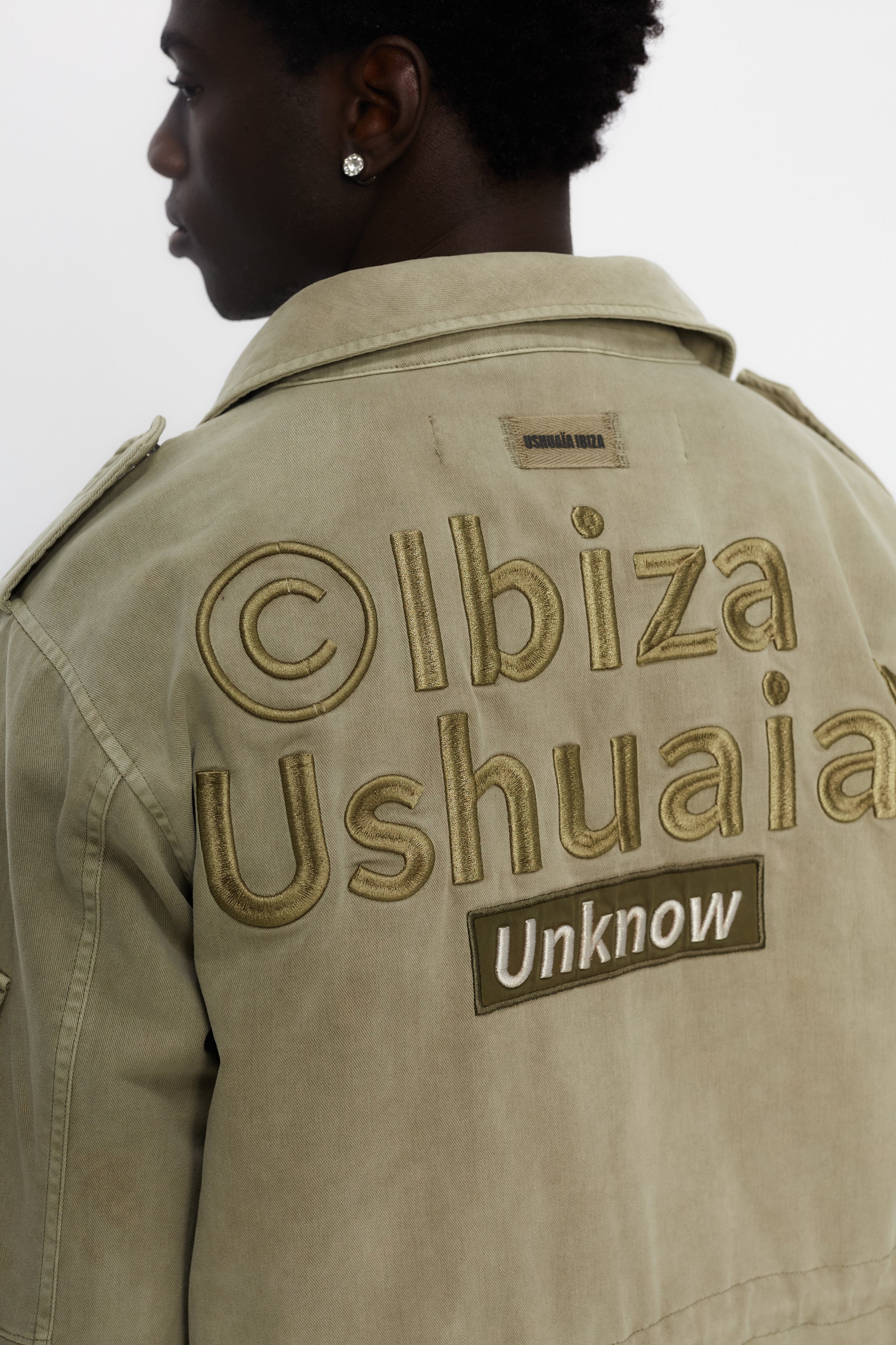 Washed twill military jacket with shirt collar and long sleeves with adjustable cuff with button. Central zip closure with adjustable drawstring at the waist. Patch pockets and flap on the front and sleeve. Combination of patches and embroidered application on front and back. Custom label detail on the back.